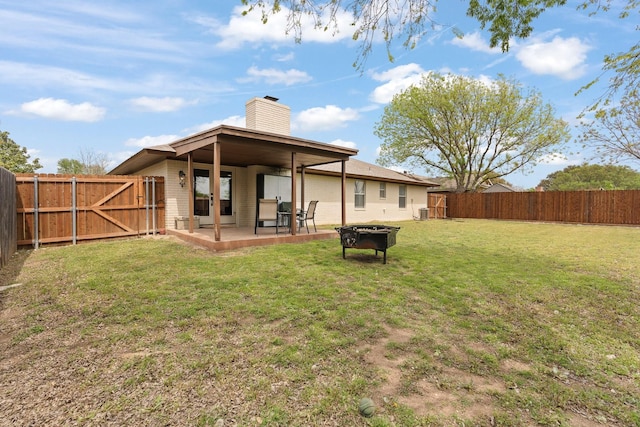 back of house featuring a gate, a chimney, a fenced backyard, a patio, and a yard