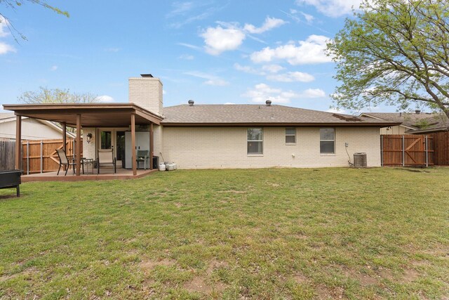back of house featuring a chimney, a fenced backyard, brick siding, a lawn, and a patio area