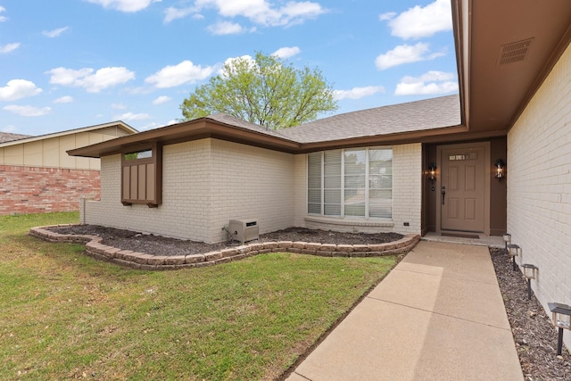 doorway to property featuring brick siding, a shingled roof, visible vents, and a yard