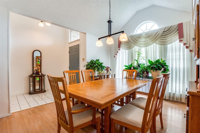dining space with light wood-style floors, a textured ceiling, and lofted ceiling