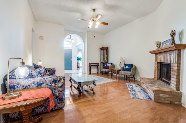 living area featuring a fireplace, a textured ceiling, ceiling fan, arched walkways, and wood finished floors