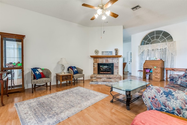 living area with wood finished floors, ceiling fan, a fireplace, and visible vents