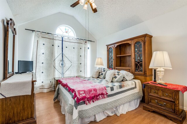 bedroom with ceiling fan, light wood finished floors, vaulted ceiling, and a textured ceiling