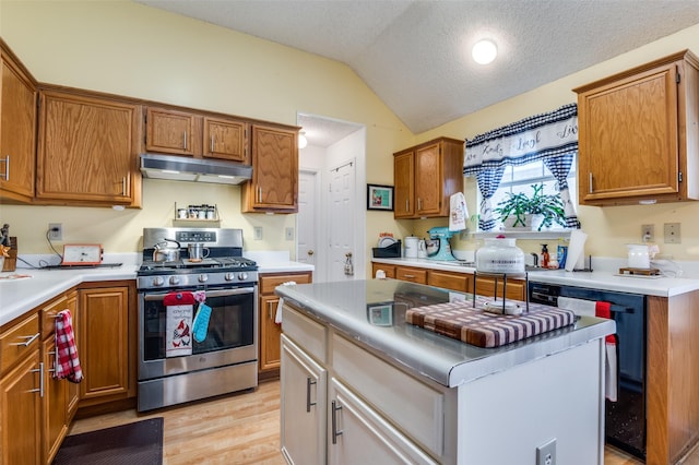 kitchen featuring light wood-style flooring, brown cabinetry, under cabinet range hood, lofted ceiling, and stainless steel gas range oven