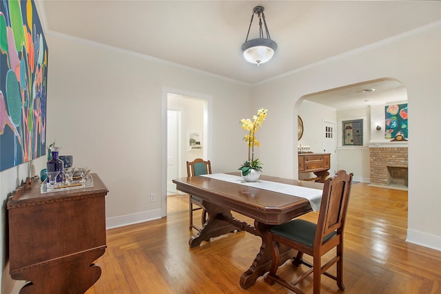 dining space featuring baseboards, arched walkways, ornamental molding, and a brick fireplace