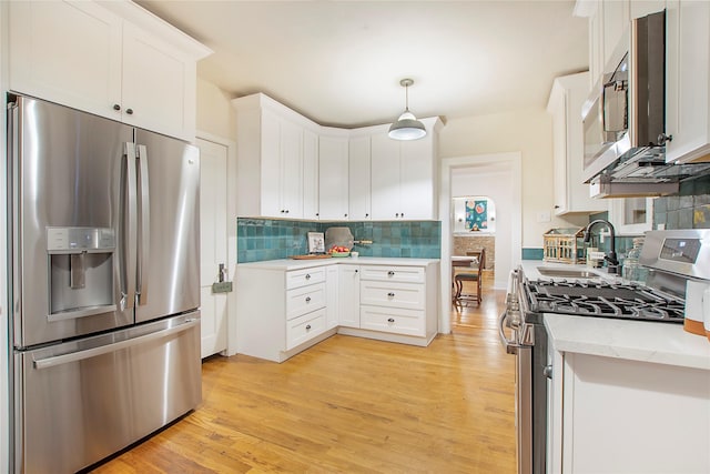 kitchen with white cabinetry, light wood-type flooring, stainless steel appliances, decorative backsplash, and a sink