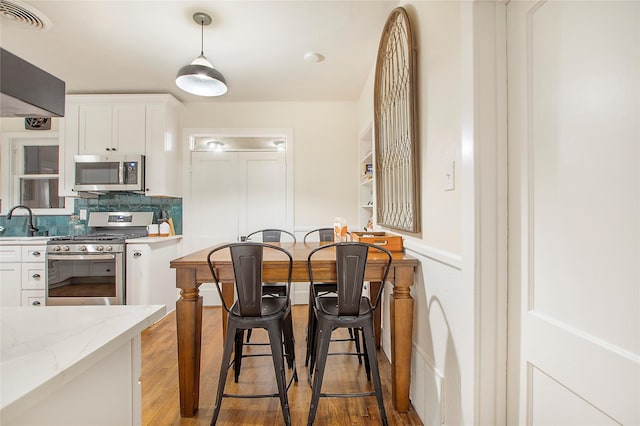 kitchen with tasteful backsplash, appliances with stainless steel finishes, visible vents, white cabinets, and light wood-style floors