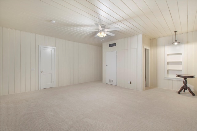 carpeted empty room with a ceiling fan, built in shelves, and visible vents