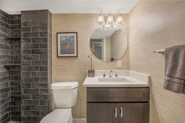 bathroom with toilet, tiled shower, and vanity