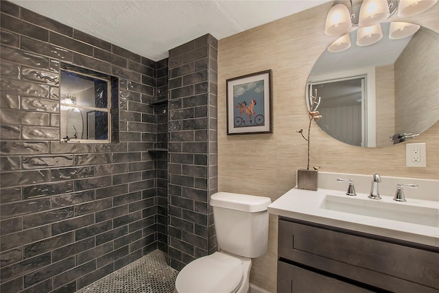 full bathroom featuring toilet, vanity, a tile shower, and a textured ceiling