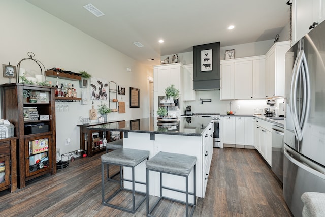 kitchen with a kitchen island, a kitchen bar, dark wood-style floors, stainless steel appliances, and dark countertops