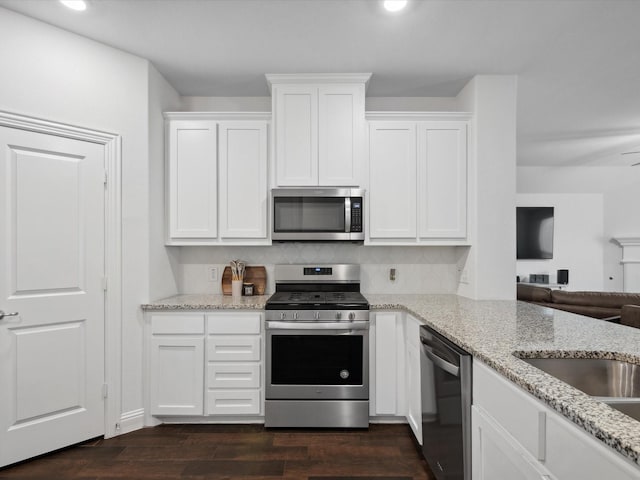 kitchen with light stone counters, open floor plan, stainless steel appliances, white cabinets, and dark wood-style flooring