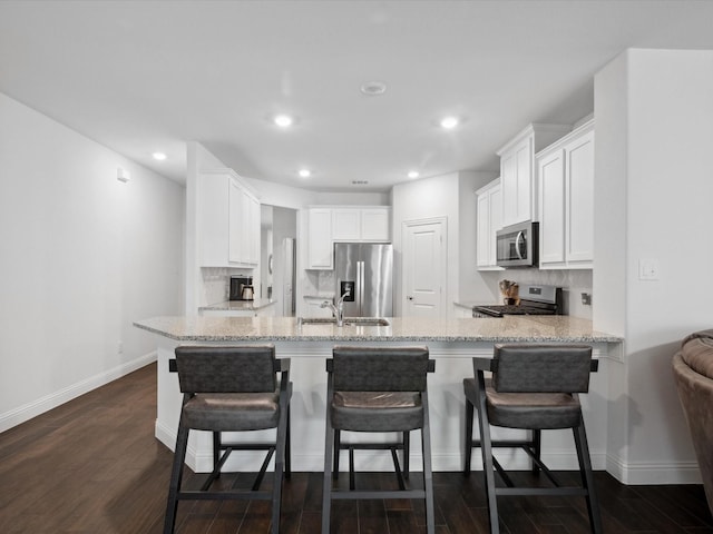 kitchen featuring decorative backsplash, stainless steel appliances, baseboards, a peninsula, and white cabinetry