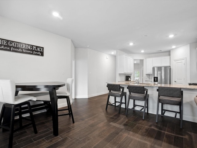 kitchen featuring white cabinets, a kitchen breakfast bar, light stone countertops, stainless steel fridge, and dark wood-style flooring