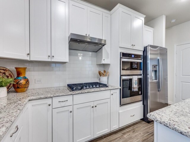 kitchen featuring light wood-style flooring, stainless steel appliances, white cabinetry, decorative backsplash, and under cabinet range hood