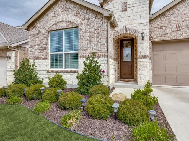 property entrance with concrete driveway, brick siding, stone siding, and a garage