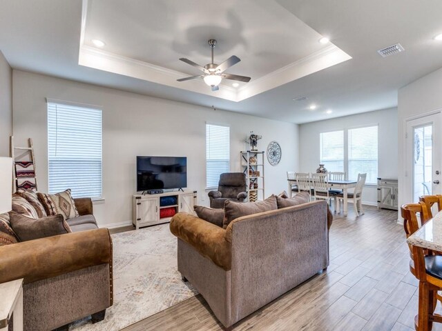 living area with ceiling fan, wood finished floors, a tray ceiling, visible vents, and ornamental molding