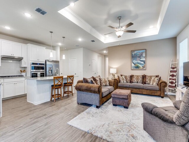 living area with recessed lighting, a tray ceiling, ornamental molding, and light wood-style flooring