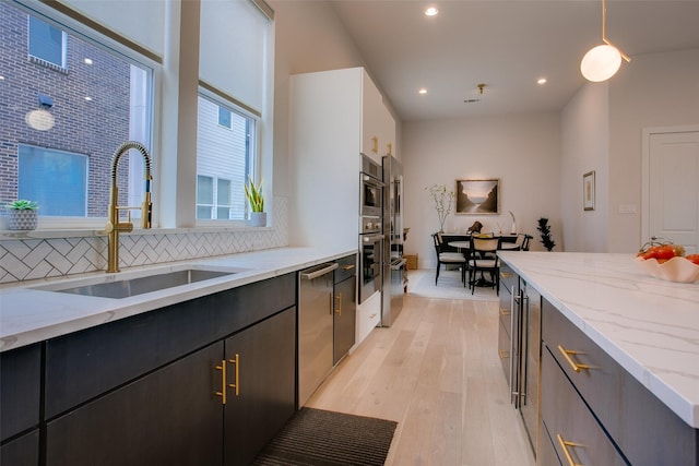 kitchen with a sink, light stone countertops, tasteful backsplash, stainless steel dishwasher, and light wood-type flooring