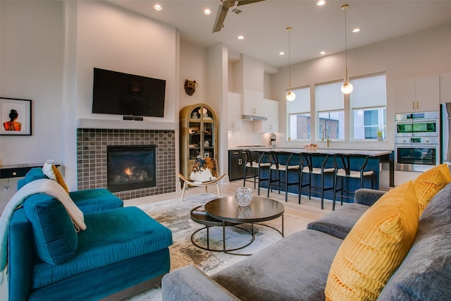 living room featuring a tiled fireplace, visible vents, light wood-style floors, a towering ceiling, and recessed lighting