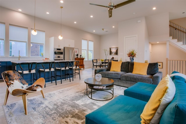 living room with stairway, recessed lighting, a towering ceiling, light wood finished floors, and a ceiling fan