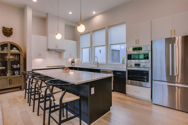 kitchen with a kitchen bar, stainless steel appliances, under cabinet range hood, pendant lighting, and a center island