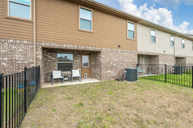 rear view of property featuring central air condition unit, fence, a patio, brick siding, and a yard