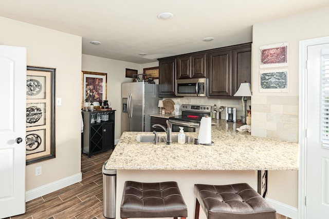 kitchen featuring dark brown cabinetry, a breakfast bar area, appliances with stainless steel finishes, a peninsula, and wood tiled floor