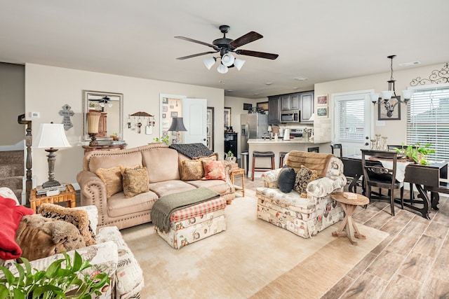 living room with light wood finished floors, ceiling fan with notable chandelier, and visible vents