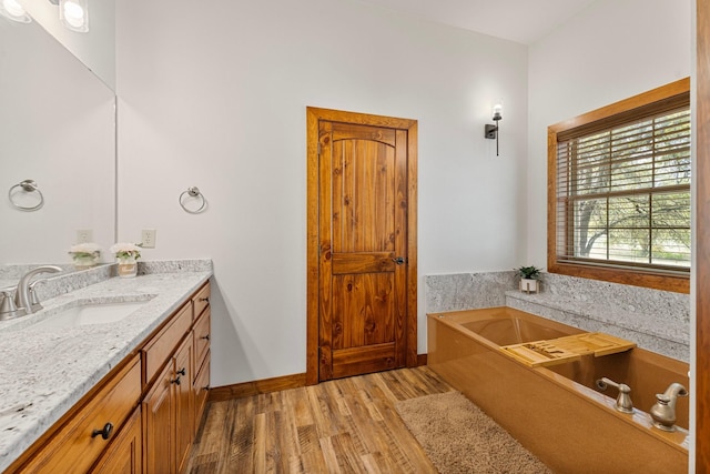 bathroom featuring baseboards, wood finished floors, vanity, and a garden tub