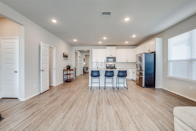kitchen featuring light countertops, appliances with stainless steel finishes, white cabinetry, open floor plan, and a breakfast bar area
