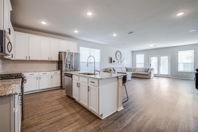 kitchen featuring open floor plan, stainless steel appliances, dark wood finished floors, a sink, and light stone counters