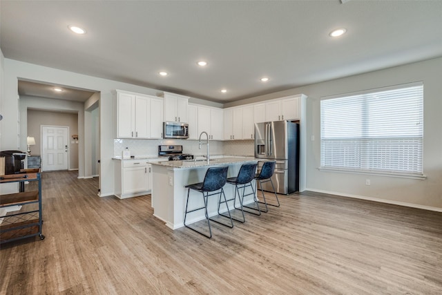 kitchen featuring a kitchen breakfast bar, appliances with stainless steel finishes, a center island with sink, light wood-style flooring, and white cabinets
