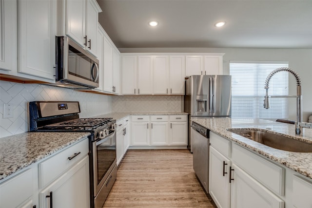 kitchen with a sink, backsplash, white cabinetry, appliances with stainless steel finishes, and light wood-style flooring