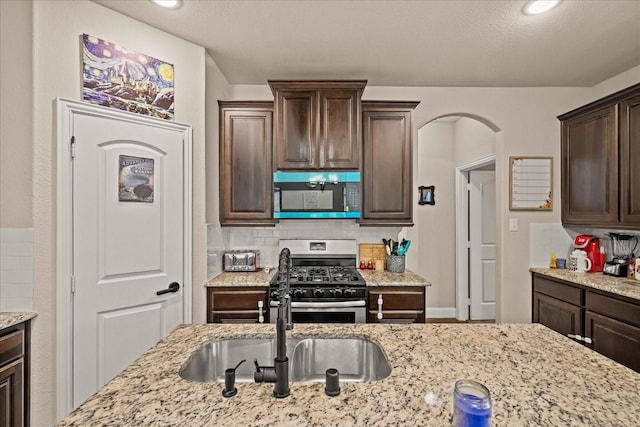 kitchen with tasteful backsplash, a sink, stainless steel gas range, dark brown cabinetry, and light stone countertops