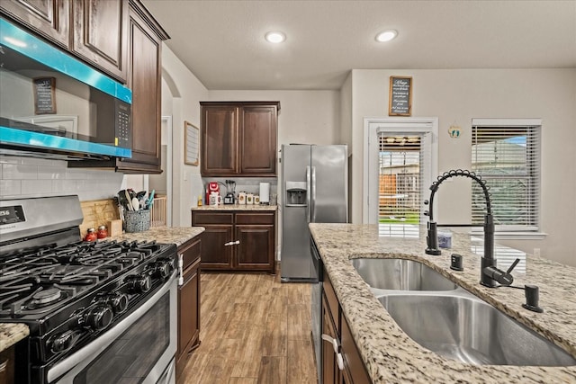 kitchen with tasteful backsplash, light wood-type flooring, dark brown cabinets, appliances with stainless steel finishes, and a sink