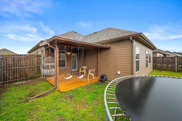 back of house featuring roof with shingles, a fenced backyard, a deck, and a lawn