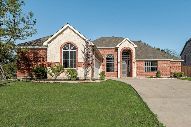 single story home with a shingled roof, a front yard, stone siding, and brick siding