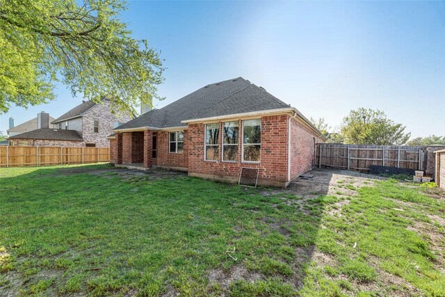 rear view of property featuring a shingled roof, brick siding, a fenced backyard, and a lawn