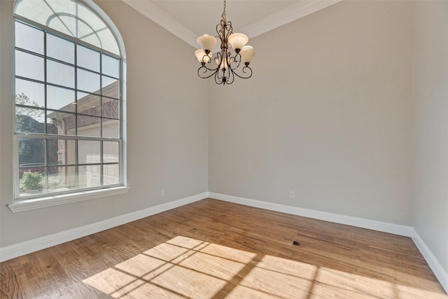 unfurnished room featuring crown molding, wood finished floors, baseboards, and a notable chandelier