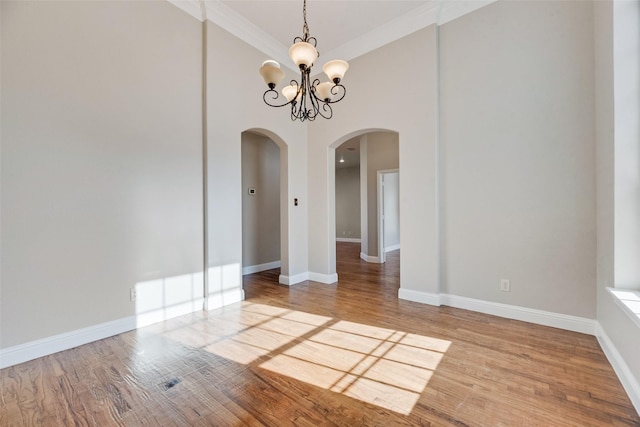 unfurnished dining area featuring an inviting chandelier, arched walkways, a towering ceiling, wood finished floors, and baseboards