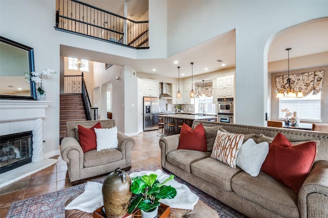 1179 Marquette Dr, Frisco, TX 75033 - living room featuring a chandelier, arched walkways, stairway, a tiled fireplace, and a towering ceiling