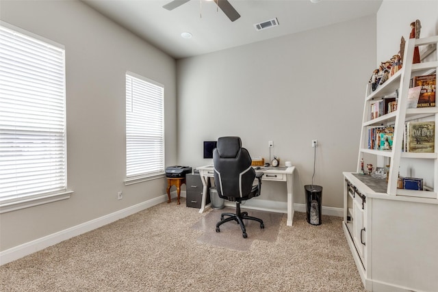 home office with a ceiling fan, visible vents, light carpet, and baseboards