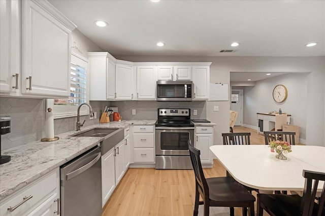 kitchen with a sink, white cabinets, light wood-style floors, and appliances with stainless steel finishes