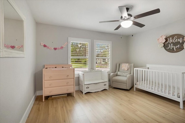 bedroom with light wood finished floors, baseboards, a crib, and a ceiling fan