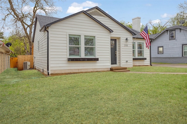 bungalow-style home featuring central air condition unit, fence, a front yard, a shingled roof, and a chimney