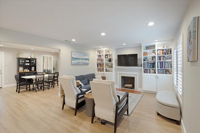 living area with light wood-style flooring, a fireplace with flush hearth, baseboards, and recessed lighting