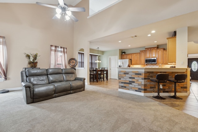 living room with a ceiling fan, light carpet, baseboards, a towering ceiling, and recessed lighting