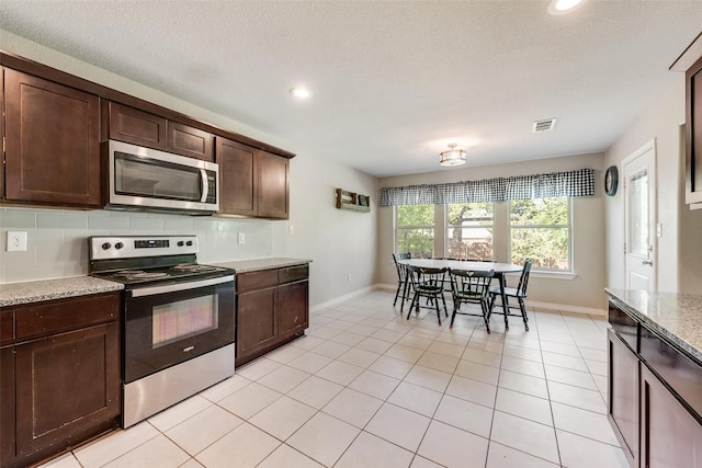 207 Shady Oaks Dr, Runaway Bay, TX 76426 - kitchen with visible vents, light tile patterned floors, appliances with stainless steel finishes, dark brown cabinetry, and decorative backsplash