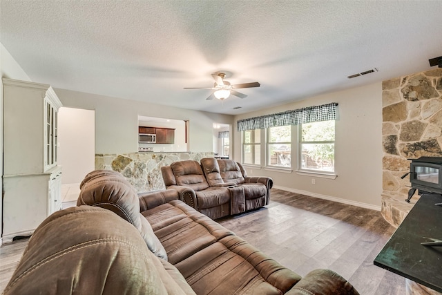 207 Shady Oaks Dr, Runaway Bay, TX 76426 - living area with visible vents, a wood stove, a ceiling fan, a textured ceiling, and light wood-style flooring